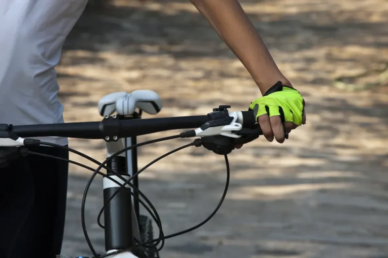 Gloved hand on a flat mountain bike handlebar with the brake lever, shifter and cables beside the grip