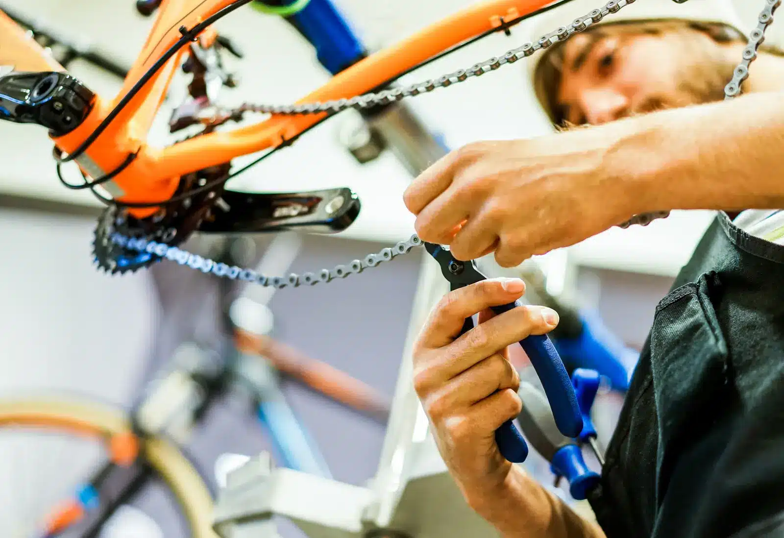 Mechanic using master link pliers on a bike chain while sizing it on a mountain bike in a repair stand