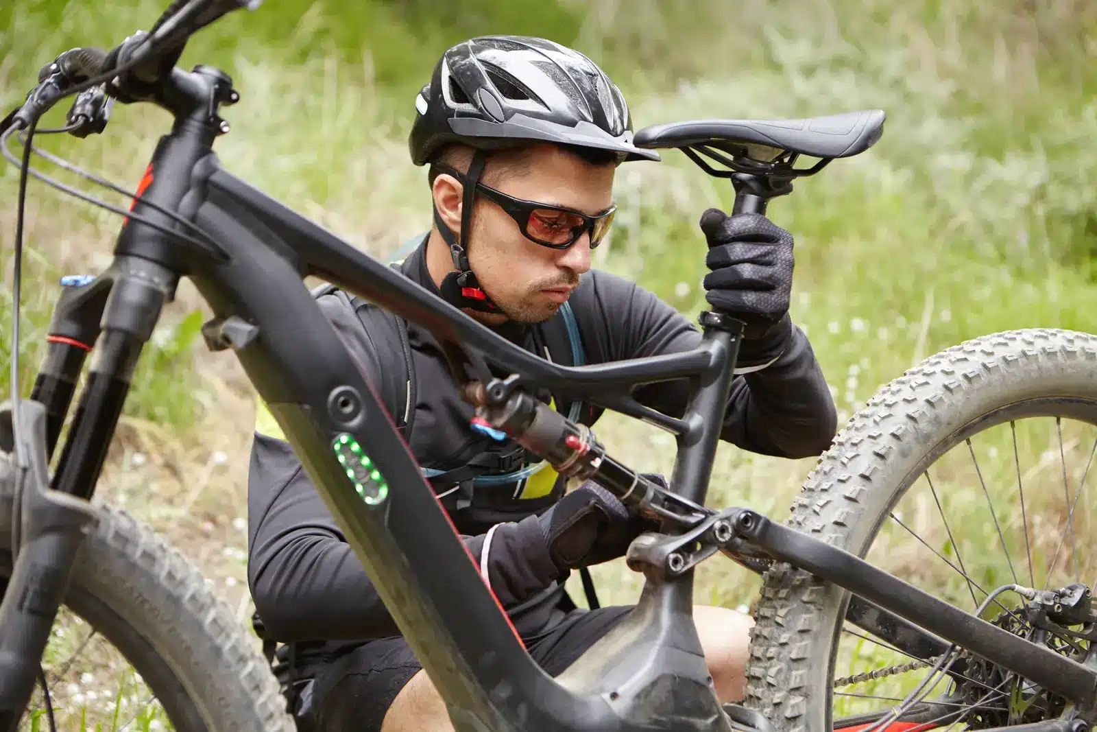 Mountain biker checking the seatpost and saddle on a full-suspension e-MTB on a grassy trail