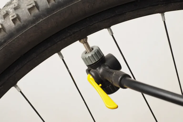 Bicycle pump head with a yellow locking lever clamped onto a threaded valve stem on a mountain bike wheel