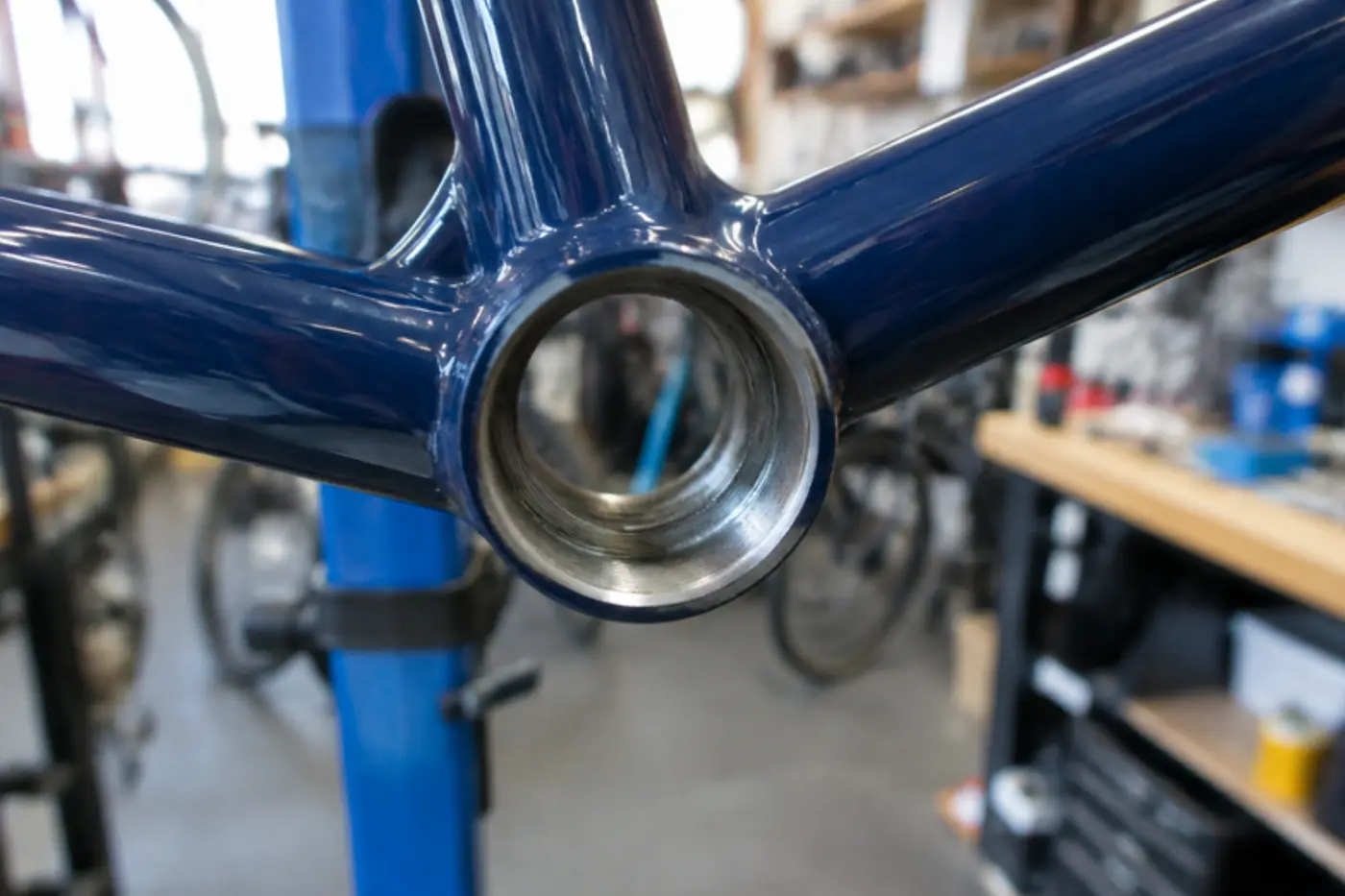 Close-up looking into an empty threaded bottom bracket shell on a blue bike frame, internal threads visible