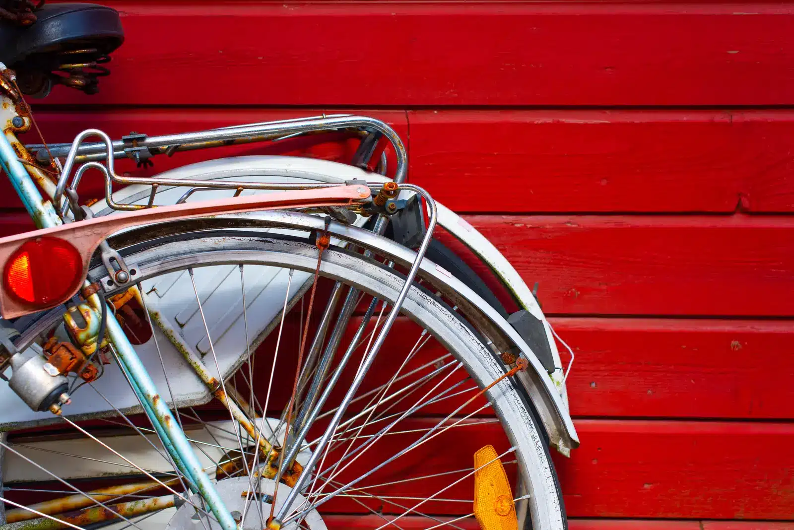 Rear wheel of an older city bike with a steel fender, rack and reflector against a red wall